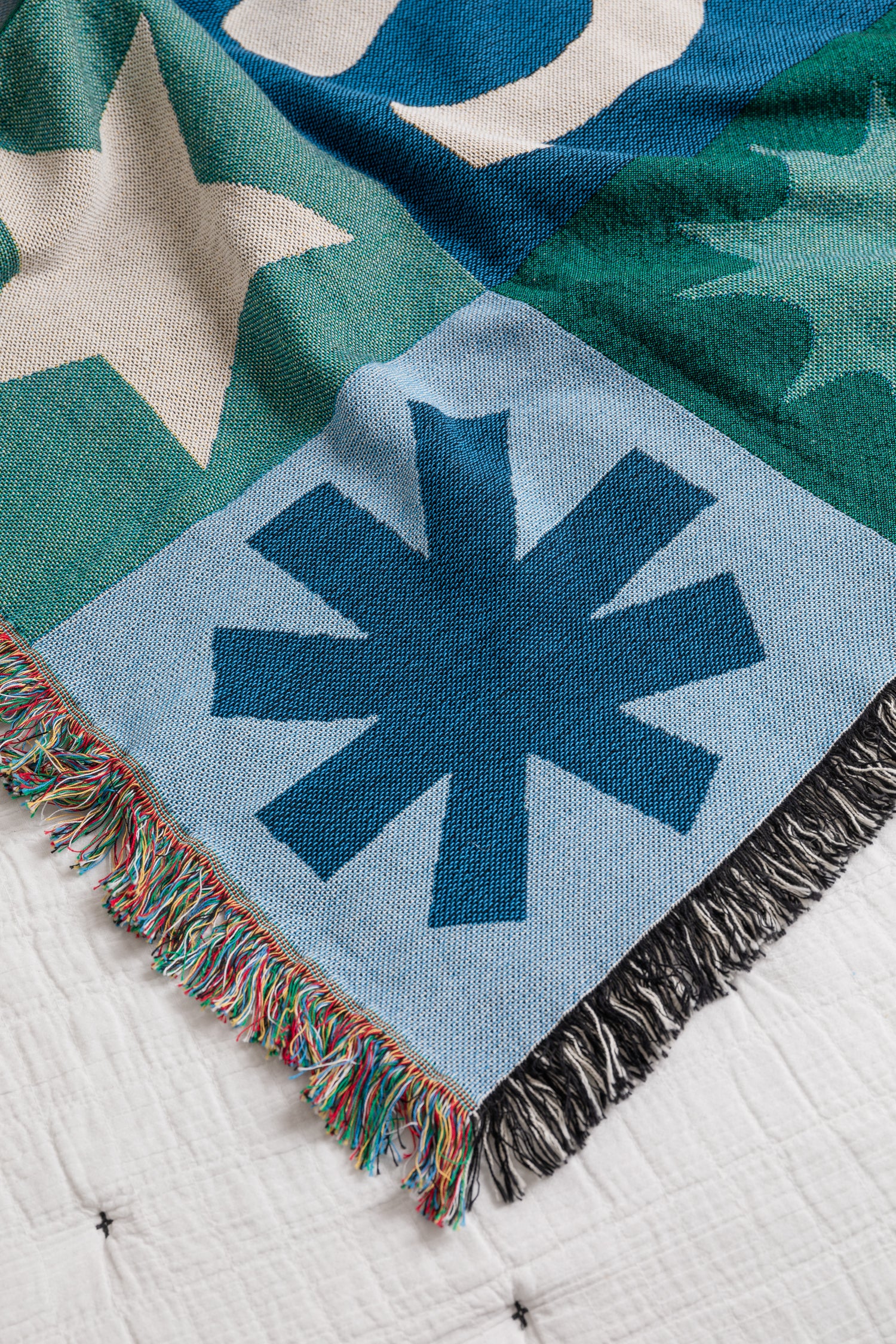 Colorful blanket with geometric patterns on a white bedspread.