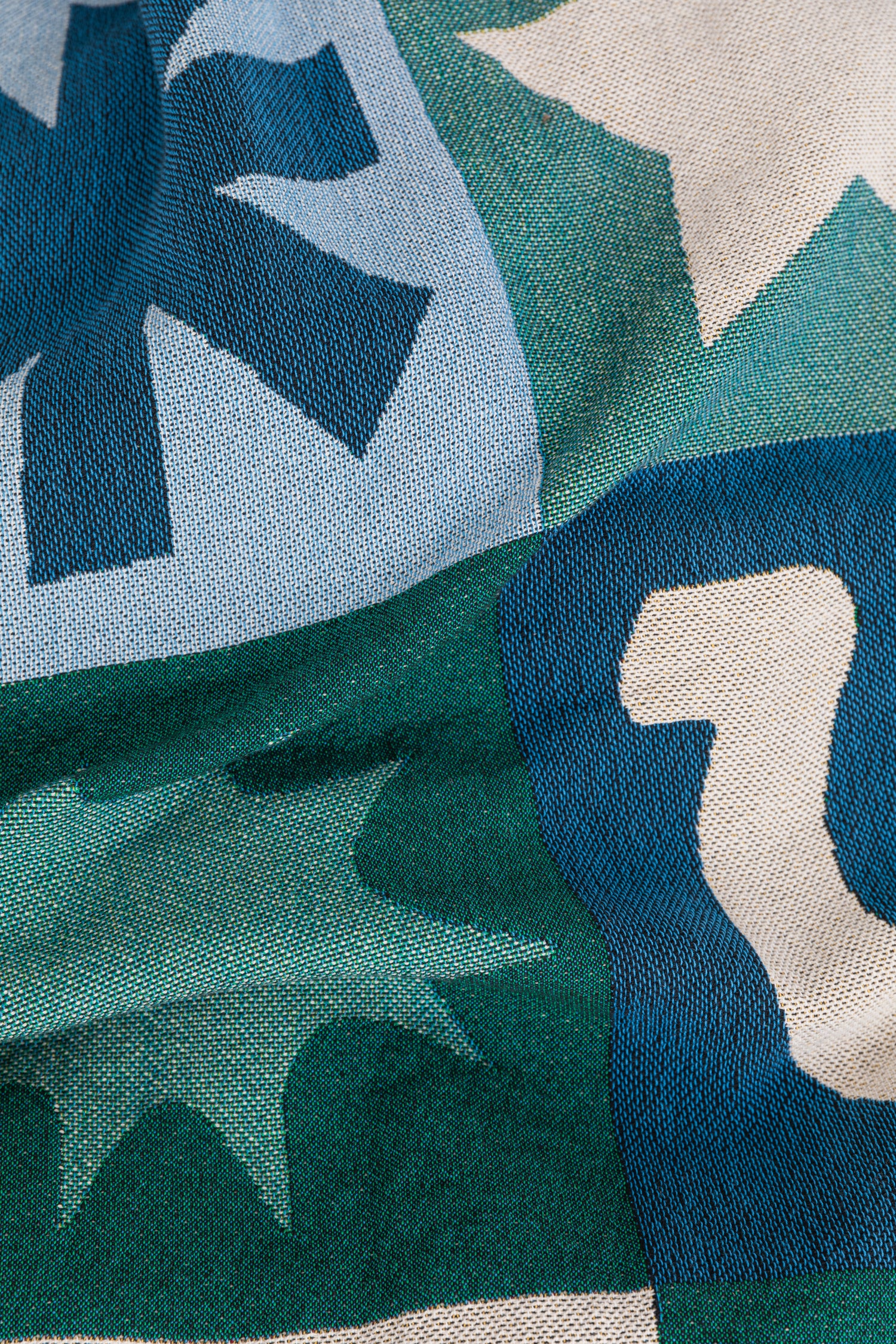 Close-up of a patterned woven blanket with geometric shapes in blue, green, and off-white.
