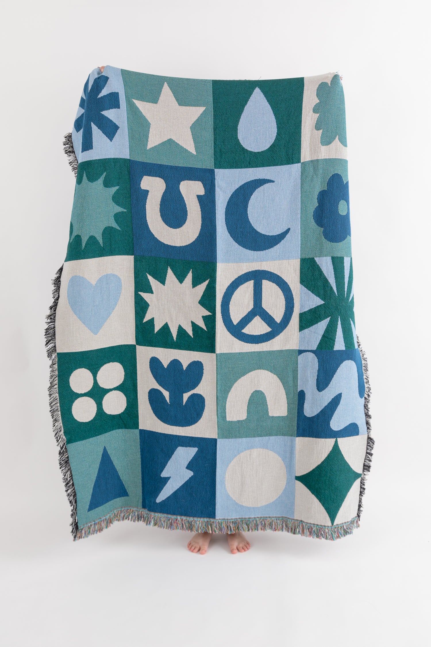 A patchwork throw blanket with geometric and folk patterns in blue, green, and off-white hues, featuring a fringe border.