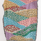Colorful woven throw blanket with a floral pattern and geometric designs with a fringe border