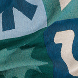 Close-up of a patterned woven blanket with geometric shapes in blue, green, and off-white.